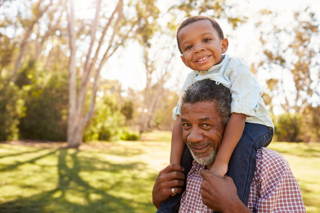 A child sits on his grandfather's shoulders, smiling.