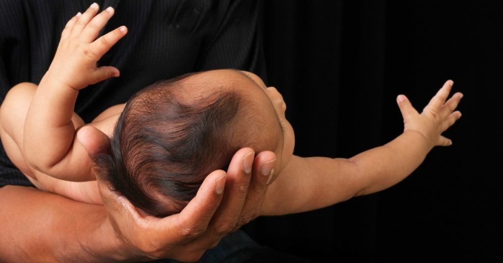 A man holds a small baby in one hand